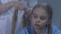 Medical worker braiding upset girl hair, child feeling homesick in hospital