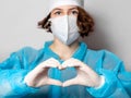 Medical worker in a disposable mask and a lab coat makes a heart sign. Gray homogeneous background. Conceptual photo: doctors on