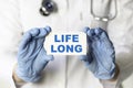 A medical worker in gloves holds a card with the words LIFE LONG. Medical concept