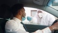 Medical worker in personal protective equipment swabbing a person in a car drive through