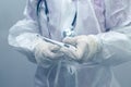 A medical worker in a protective suit holds an electronic thermometer for measuring body temperature. Close-up shot, cold toning