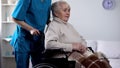 Medical worker taking care about upset senior lady in wheelchair, rehabilitation