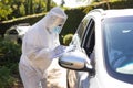 Medical worker wearing ppe suit taking notes talking to senior african american woman sitting in car Royalty Free Stock Photo