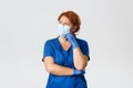 Medical workers, coronavirus concept. Confused and thoughtful female redhead doctor, nurse in scrubs, face mask and