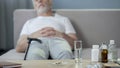 Medicaments standing on the table, ill lonely grandfather sleeping on couch
