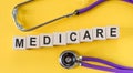 Medicare word written on cube shape wooden blocks on yellow table with stethoscope Royalty Free Stock Photo