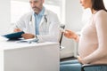 Medication in pregnancy. Male doctor prescribing medicines pills for young pregnant lady, female patient holding tablets