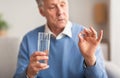 Senior Man Holding A Pill And Water Sitting On Sofa