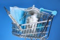 Blue shopping cart with thermometer, medical mask, jar of pills on a blue background. Covid-19 Royalty Free Stock Photo