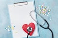 Medicine clipboard, stethoscope, drug pills, and red shape of heart on blue background top view. Healthy and cardiology concept. Royalty Free Stock Photo