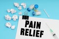 On a blue background, a syringe, medicine, white crumpled pieces of paper and a sheet with the inscription - PAIN RELIEF Royalty Free Stock Photo