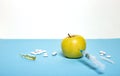 Medicine concept with fresh injured apple, tablets, ampoule and syringe. Genetically modified fruit on light blue background