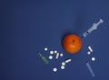 Medicine concept with injected mandarin, tablets, ampoule and syringe. Genetically modified fruit on classic blue background