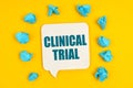 On a yellow background, blue pieces of paper and a sign with the inscription - CLINICAL TRIAL