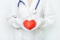 Medicine doctor close up in white coat and gloves holding red heart