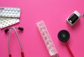 Medicine flat lay of red stethoscope, pills blisters, container for drugs and pulse oximeter on pink background with copyspace.