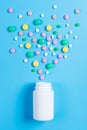 Medicine green, yellow and pink pills or capsules and white bottle on a blue background Royalty Free Stock Photo