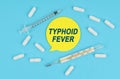 On a blue background, there are pills, a thermometer and a sticker with the inscription TYPHOID FEVER