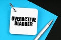 On the black surface lies blue paper, a pen and a notebook with the inscription - Overactive Bladder