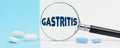 On a blue and white background, there are pills and a magnifying glass, inside of which it is written - GASTRITIS