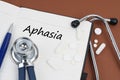 On a brown surface lie pills, a pen, a stethoscope and a notebook with the inscription - aphasia
