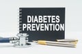 On a white background lies a stethoscope, a pen and a black notebook with the inscription - DIABETES PREVENTION