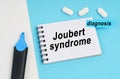 On a white and blue surface are pills, a marker and a notebook with the inscription - Joubert syndrome