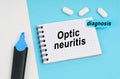 On a white and blue surface are pills, a marker and a notebook with the inscription - Optic neuritis