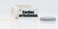 On a white reflective background, there are pills and a jar of drugs with a tag that says - Cardiac arrhythmias