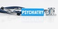 On a white reflective surface is a stethoscope and a blue Jenga with the inscription - PSYCHIATRY