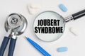 On a white surface lie pills, a pen, a stethoscope and a magnifying glass with the inscription - Joubert syndrome