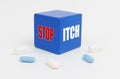 On a white surface are pills and a blue cube that says - STOP ITCH