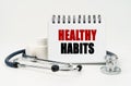 On a white table lies a stethoscope, pills and a notebook with the inscription - HEALTHY HABITS Royalty Free Stock Photo