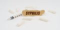 On a white table are pills, a syringe and a piece of paper with the inscription - syphilis