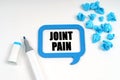 On a white surface are crumpled blue paper, a marker and a sign inside which is written - JOINT PAIN Royalty Free Stock Photo