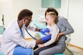Medicine, healthcare, pediatry and people concept - happy woman with her son and African American doctor with Royalty Free Stock Photo