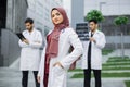 Muslim doctor with stethoscope looks at camera standing outside hospital in front of male colleagues Royalty Free Stock Photo