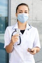 A European girl doctor in a white coat with a stethoscope and a virus mask holding several packs of pills