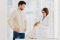 Medicine and pet care concept. Woman veterinarian wears white gown, spectalces, medic gloves, examines jack russell terrier, visit