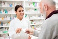 Beautiful young pharmacist selling medications to senior patient