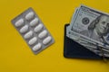 Medicine pills and 100 dollar banknote on yellow background. Healthcare insurance and medical treatment cost concept Royalty Free Stock Photo