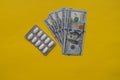 Medicine pills and 100 dollar banknote on yellow background. Healthcare insurance and medical treatment cost concept