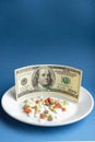 Medicines costs money. Drugs and dollars.White plate with multi-colored pills and capsules and a 100 dollar bill on a Royalty Free Stock Photo