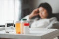 Medicines and glass of water with sick Asian woman