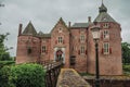 Medieval Ammersoyen Castle with its brick towers, wooden bridge and green garden on cloudy day.