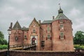 Medieval Ammersoyen Castle with its brick towers, wooden bridge and green garden on cloudy day.