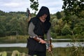 Medieval archer with black hood with the curve span before a lake and looks forwards Royalty Free Stock Photo