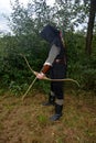 Medieval archer of the side stands with black hood and with tense bow and with arrow Royalty Free Stock Photo