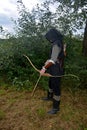 Medieval archer of the side stands with black hood and with tense bow and with arrow