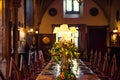 Medieval british castle interior dining table with plates, flowers and lamps. Warm light. Selective focus. copy space Royalty Free Stock Photo